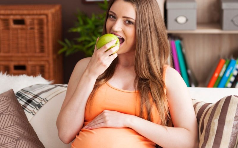 pregnant-woman-eating-apple-sofa_329181-2647