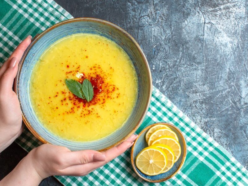 top-view-hand-holding-blue-pot-with-tasty-soup-served-with-mint-chopped-lemon-half-folded-green-stripped-towel-blue-background_140725-94738.jpg